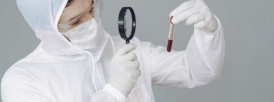 Man in protective suit and glasses in studio Corona virus theme. Man in a protective suit. Doctor looks at the blood tube.