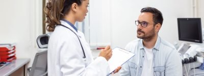 Serious man consulting with young female physician doctor at checkup meeting in hospital. Skilled general practitioner giving healthcare medical advices to patient. Serious man consulting with young female physician doctor at checkup meeting in hospital. Skilled general practitioner giving healthcare medical advices to patient.