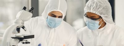 Chemist researchers during global pandemic with covid-19 checkin Scientists and microbiologists with PPE suit and face mask hold test tube and microscope in lab, finding treatment or vaccine for coronavirus infection. Covid-19, laboratory, and vaccine concept.