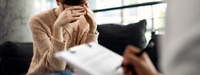 Depressed woman having psychotherapy session at doctor’s office. Sad woman holding her head in pain while having a meeting with psychotherapist.